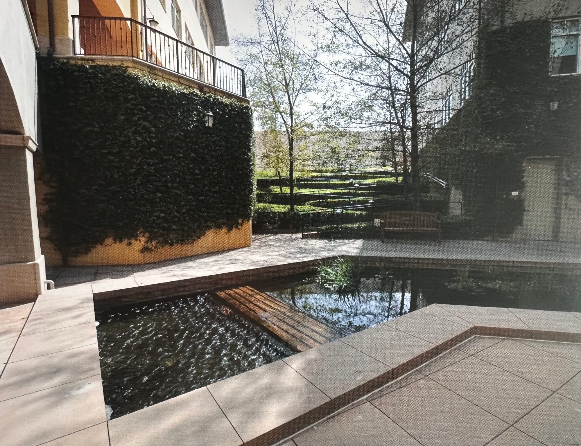 A landscaped courtyard with a zigzag path bordered by hedges and a reflecting pond, showing both the designed walkway and a faint shortcut path along its side.